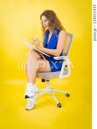 Woman writing notes with pencil on vibrant yellow background Woman writing notes with pencil on vibrant yellow background 138012435