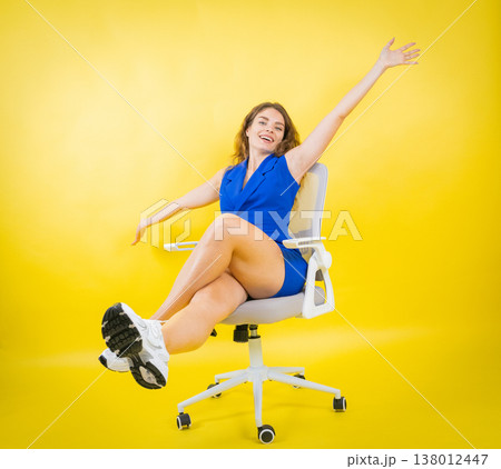 Happy woman sitting on chair against yellow wall 138012447