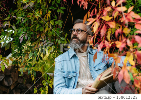 Man is enjoying a relaxing, peaceful moment at home, sitting among greenery and reading a book. 138012525