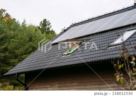 Man looking from skylight, roof window with solar panels above him. Sustainable lifestyle and green household. Man looking from skylight, roof window with solar panels above him. Sustainable lifestyle and green household. 138012530