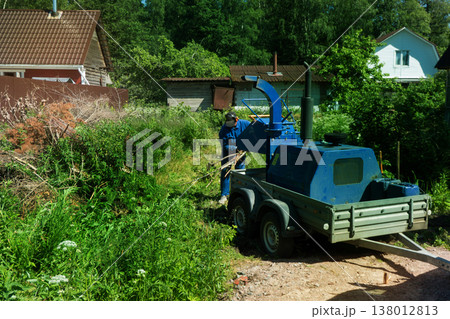 An operator loads tree branches into a wood chipper. An operator loads tree branches into a wood chipper. 138012813