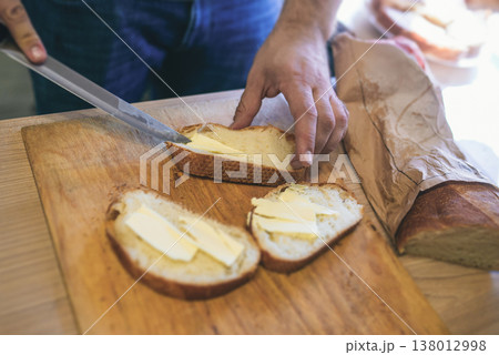 Close up of male hands spreading fresh butter on crusty bread slices using a knife Close up of male hands spreading fresh butter on crusty bread slices using a knife 138012998