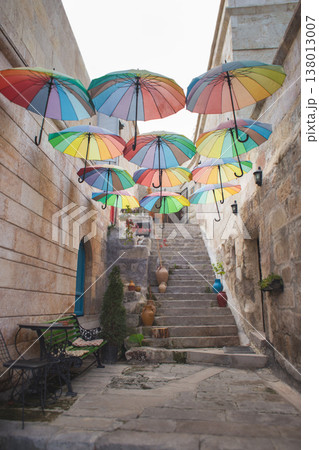 Colorful rainbow umbrellas hanging over a stone alleyway in a Turkish town 138013007