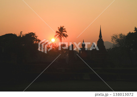 Silhouette of ancient Buddha statue and temple spires against a bright golden sunset sky Silhouette of ancient Buddha statue and temple spires against a bright golden sunset sky 138013072