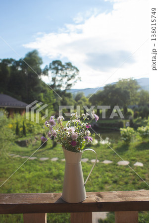 Wildflower bouquet in a rustic pitcher on a balcony overlooking a garden 138015749