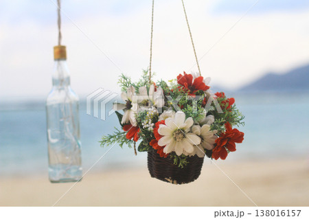 Hanging flower basket and glass bottle decoration on a beach Hanging flower basket and glass bottle decoration on a beach 138016157