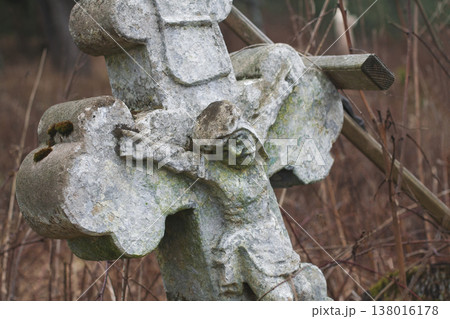 Ancient mossy stone crucifix monument standing among bare branches in a quiet winter forest Ancient mossy stone crucifix monument standing among bare branches in a quiet winter forest 138016178