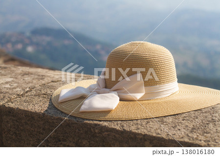 Straw sun hat with a white bow resting on a stone ledge 138016180