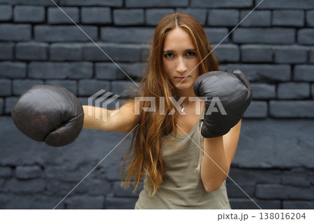Young woman in boxing gloves throwing a punch against dark brick wall Young woman in boxing gloves throwing a punch against dark brick wall 138016204