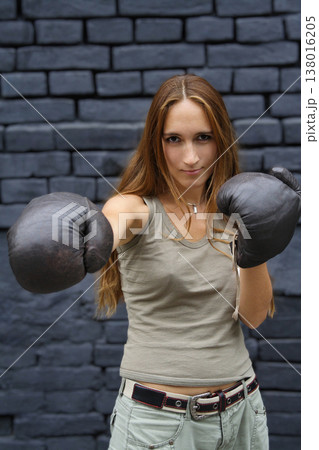 Young woman in boxing gloves throwing a punch against dark brick wall 138016205