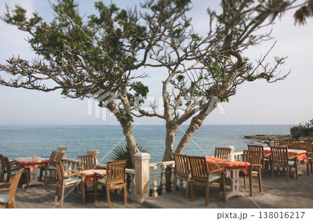Outdoor restaurant terrace with a sea view under a spreading tree 138016217