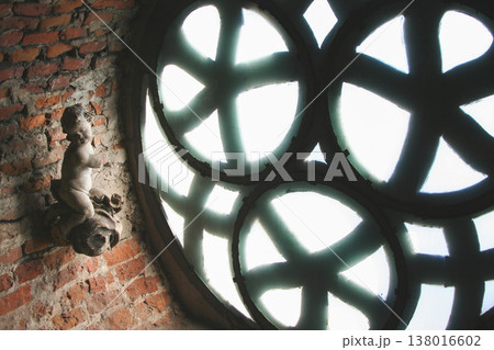 Stone cherub sculpture beside a decorative rose window in a brick wall Stone cherub sculpture beside a decorative rose window in a brick wall 138016602