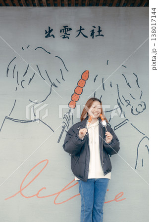 観光地でいちご飴を食べる笑顔の20代女性 観光地でいちご飴を食べる笑顔の20代女性 138017144