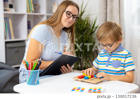 Woman Observing Young Boy Solving Puzzle at Table in Bright Room Woman Observing Young Boy Solving Puzzle at Table in Bright Room 138017236