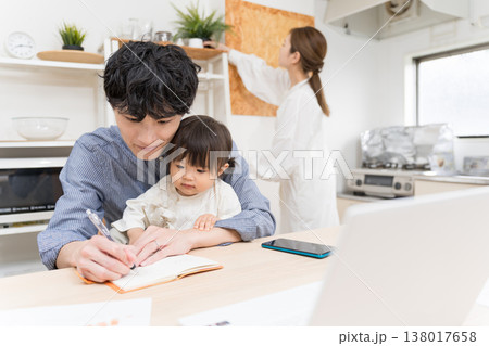 ダイニングで子どもの世話をしながらメモを取って仕事する若い父親 在宅ワークの育児風景 138017658