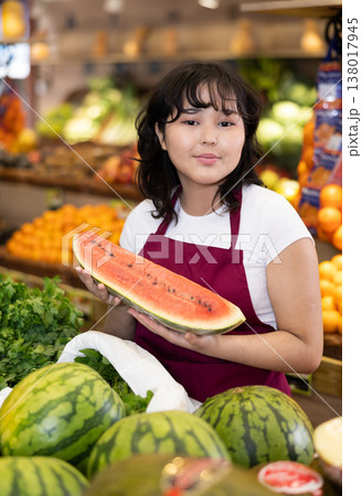 Positive girl seller of grocery supermarket with ripe watermelon in her hands Positive girl seller of grocery supermarket with ripe watermelon in her hands 138017945