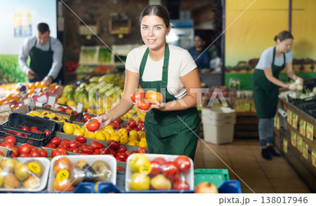 Girl seller of garden stuff store works near showcase, sorting tomato, checking goods Girl seller of garden stuff store works near showcase, sorting tomato, checking goods 138017946