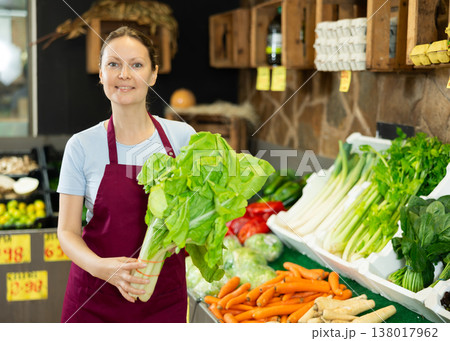 Woman seller of garden stuff store replenishing showcase, puts salad mangold on showcase Woman seller of garden stuff store replenishing showcase, puts salad mangold on showcase 138017962