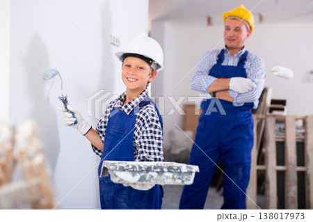 Boy in blue overalls paints the walls with paint roller Boy in blue overalls paints the walls with paint roller 138017973