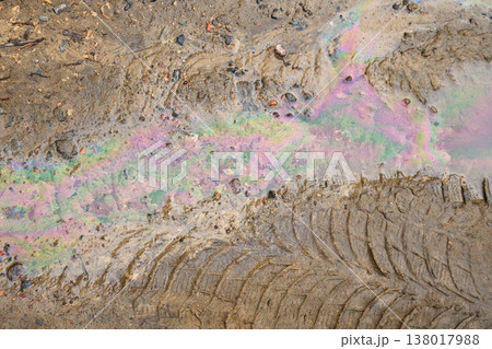 Ground showing an iridescent oil spill polluting dirty puddle with car tire tracks. A symbol of environmental contamination Ground showing an iridescent oil spill polluting dirty puddle with car tire tracks. A symbol of environmental contamination 138017988