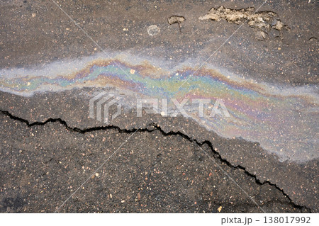 Iridescent oil slick spreading on damaged asphalt surface, reflecting vibrant rainbow colors, highlighting an environmental pollution issue 138017992
