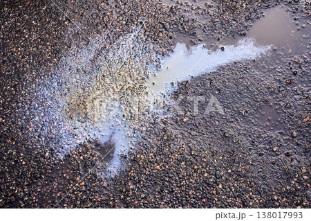 Iridescent oil slick spreading in a puddle on wet asphalt, showing environmental pollution and chemical waste 138017993