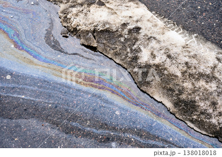 Oil slick creating iridescent rainbow pattern on wet asphalt road next to dirty melting snow Oil slick creating iridescent rainbow pattern on wet asphalt road next to dirty melting snow 138018018