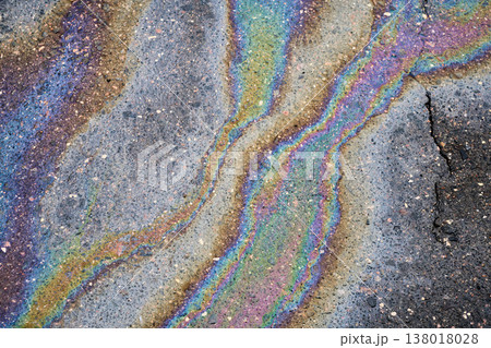 Iridescent oil spill on dark asphalt forming abstract patterns, colorful liquid reflects light with a rainbow effect, indicating pollution Iridescent oil spill on dark asphalt forming abstract patterns, colorful liquid reflects light with a rainbow effect, indicating pollution 138018028