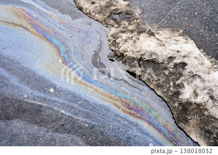 Glistening oil slick displaying vivid colors on the damp pavement, depicting the consequences of pollution, environmental harm, and intricate abstract designs Glistening oil slick displaying vivid colors on the damp pavement, depicting the consequences of pollution, environmental harm, and intricate abstract designs 138018032