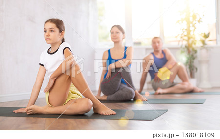 Pleasant preteen girl practicing half lord of the fishes pose of yoga with her family 138018109