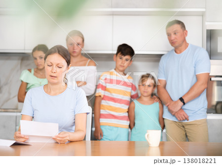 Upset mother reads and looks through financial documents. Sad wife with children in background 138018221