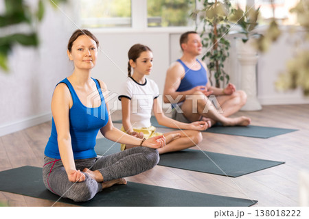 Happy middle-aged woman practicing lotus pose of yoga with her family 138018222