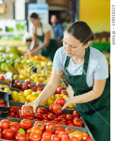 Female seller lays out ripe tomatoes on the counter of grocery supermarket 138018223
