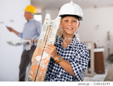 Portrait of positive boy carrying stepladder in construction site Portrait of positive boy carrying stepladder in construction site 138018245