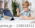 Young boy with headphones studying at desk with tablet and notebook 138018312