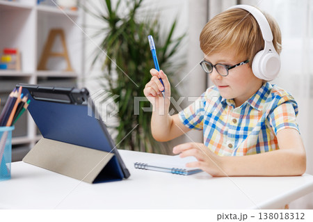 Young boy with headphones studying at desk with tablet and notebook Young boy with headphones studying at desk with tablet and notebook 138018312