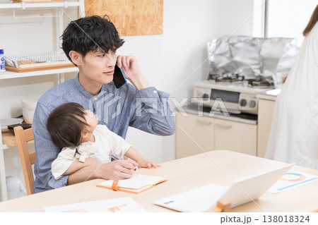 ダイニングで子どもの世話をしながら電話で仕事する若い父親 在宅ワークの育児風景 ダイニングで子どもの世話をしながら電話で仕事する若い父親 在宅ワークの育児風景 138018324