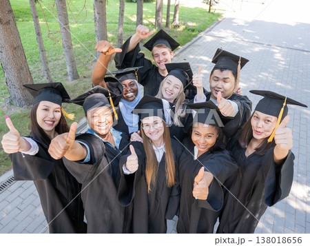 Students of different nationalities in graduation gowns give thumbs up. Students of different nationalities in graduation gowns give thumbs up. 138018656