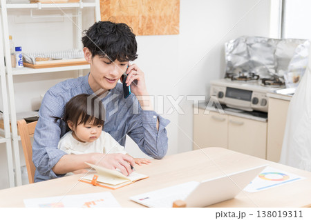 ダイニングで子どもの世話をしながら電話で仕事する若い父親 在宅ワークの育児風景 138019311