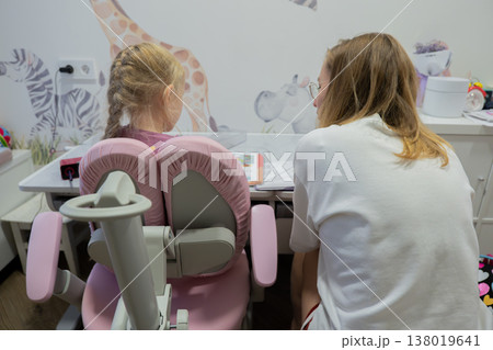 Parent guiding child at study chair, mother leans over pink ergonomic seat while child works on paper, animal-print wallpaper and tidy desk area, calm nurturing atmosphere with collaborative focus Parent guiding child at study chair, mother leans over pink ergonomic seat while child works on paper, animal-print wallpaper and tidy desk area, calm nurturing atmosphere with collaborative focus 138019641