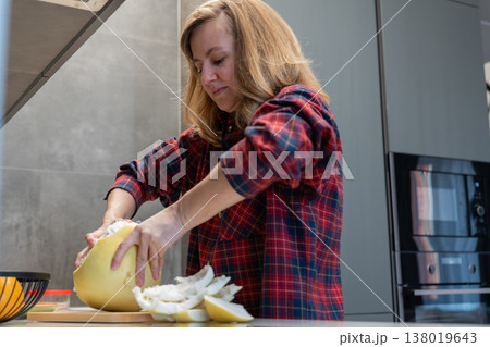 Woman peeling pomelo on countertop in modern kitchen wearing red plaid shirt removing pith and peel arranging juicy segments on board focused home cook preparing healthy snack soft daylight stainless Woman peeling pomelo on countertop in modern kitchen wearing red plaid shirt removing pith and peel arranging juicy segments on board focused home cook preparing healthy snack soft daylight stainless 138019643