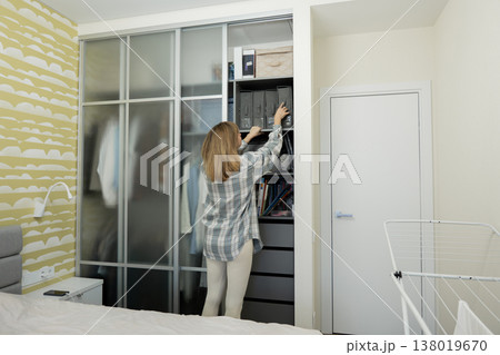 Woman arranges closet storage units, Woman methodically places labeled containers on closet shelf, Sia women carefully arrange seasonal belongings using labeled boxes in closet environment Woman arranges closet storage units, Woman methodically places labeled containers on closet shelf, Sia women carefully arrange seasonal belongings using labeled boxes in closet environment 138019670