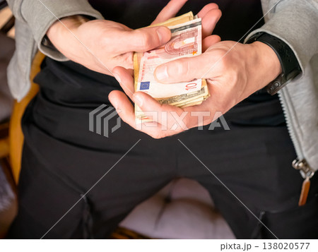 Man holding stack of Euro banknotes in hand. Counting paper money for financial transaction. Wealth, savings and investment concept. Economic growth and commercial banking operations. Man holding stack of Euro banknotes in hand. Counting paper money for financial transaction. Wealth, savings and investment concept. Economic growth and commercial banking operations. 138020577