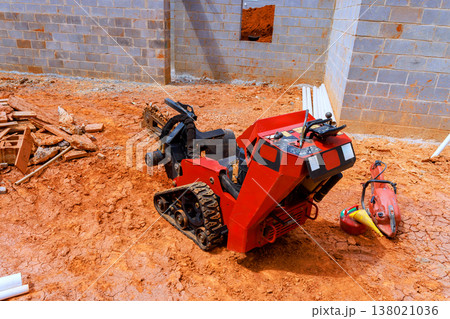 Small construction digging machine sits on dirt surface at building site with bricks pipes nearby Small construction digging machine sits on dirt surface at building site with bricks pipes nearby 138021036