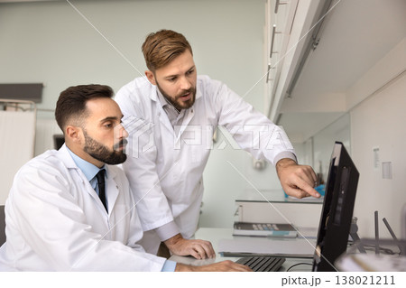 Professional team two male doctors analyzing files on pc screen Professional team two male doctors analyzing files on pc screen 138021211