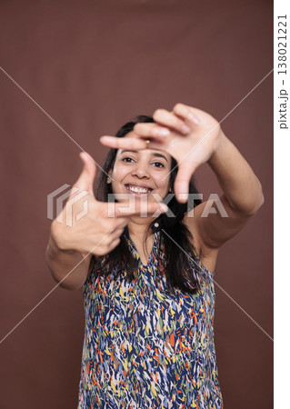 Smiling indian woman making photo frame gesture with fingers, looking at camera. Cheerful photographer posing portrait, front view studio medium shot, photography, imaginable photoshoot 138021221