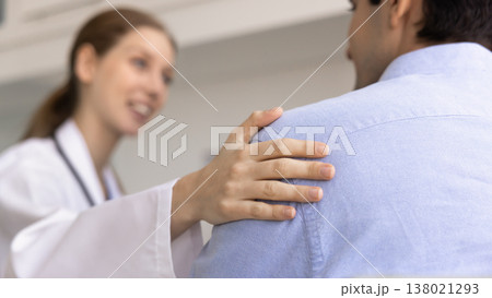 Compassionate female doctor gently touches male patient shoulder 138021293