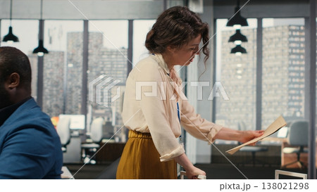 Workplace support employee moves a delivery cart stacked with folders and contracts, helping african american administrator bringing stack of archived documents for accounting tasks. Camera B. Workplace support employee moves a delivery cart stacked with folders and contracts, helping african american administrator bringing stack of archived documents for accounting tasks. Camera B. 138021298
