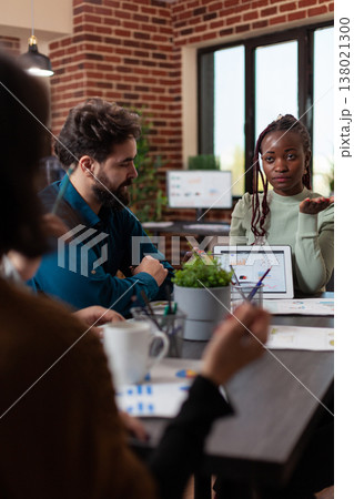 African american businesswoman showing marketing graphs to businesspeople explaining company turnover during business meeting in startup office. Diverse team working at financial project 138021300