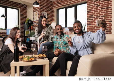 African american adult woman taking cell phone picture with asian, caucasian friends at apartment gathering. Multiple nationalities people posing for photo, drinking wine, eating snacks. African american adult woman taking cell phone picture with asian, caucasian friends at apartment gathering. Multiple nationalities people posing for photo, drinking wine, eating snacks. 138021332